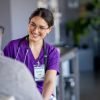 A female doctor of Hispanic decent, talks with her senior male patient during a routine check-up. She is wearing purple scrubs and smiling as she talks with the gentleman.